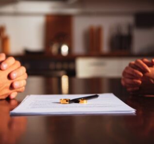 couple sitting at table with clenched hands near divorce documents