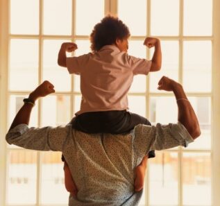 Back side view young african american father holding on shoulders little preschool funny kid son, showing biceps