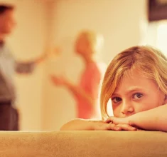 Little girl looking unhappy as her parents argue in the background. First Custody Hearing